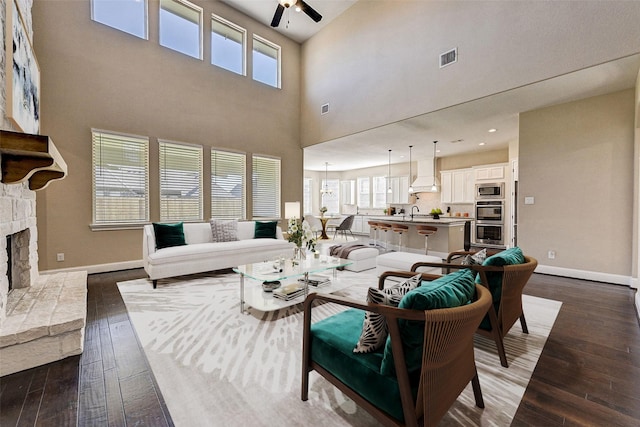 living room featuring dark hardwood / wood-style flooring, ceiling fan, a fireplace, and a high ceiling