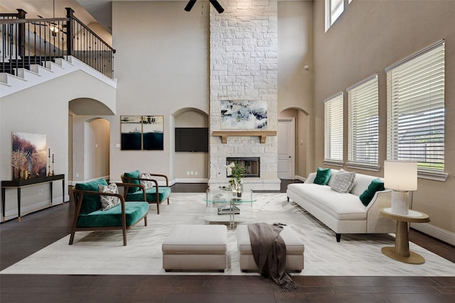 living room with ceiling fan, a fireplace, a towering ceiling, and hardwood / wood-style floors