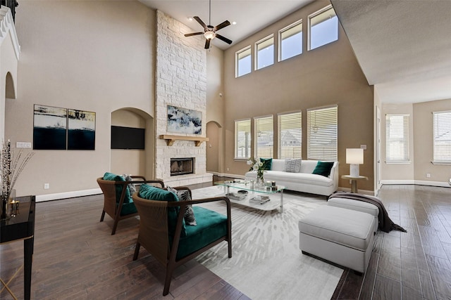 living room featuring a high ceiling, dark hardwood / wood-style flooring, a stone fireplace, and ceiling fan