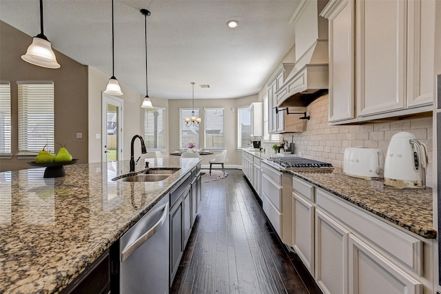 kitchen with light stone countertops, appliances with stainless steel finishes, decorative backsplash, sink, and decorative light fixtures