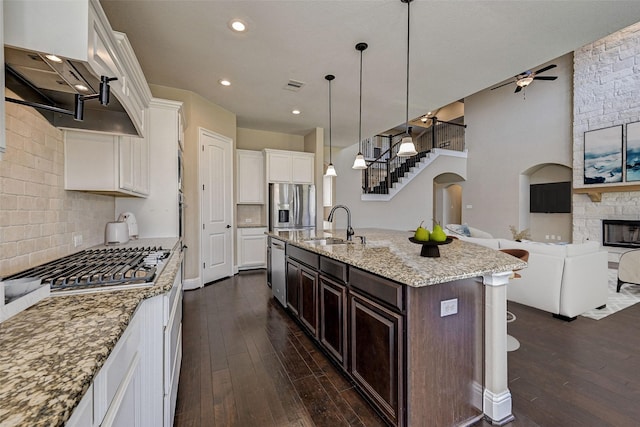 kitchen with dark brown cabinetry, backsplash, a kitchen island with sink, white cabinets, and appliances with stainless steel finishes