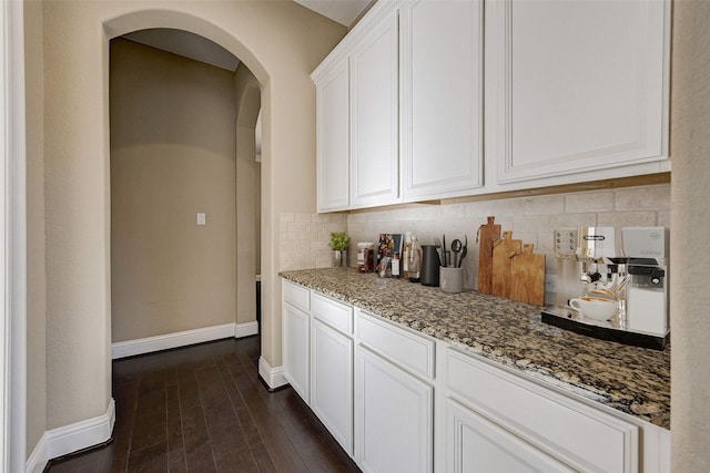 kitchen with tasteful backsplash, white cabinetry, dark wood-type flooring, and light stone counters