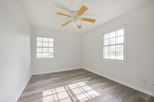 spare room featuring ceiling fan, a healthy amount of sunlight, a textured ceiling, and light hardwood / wood-style flooring