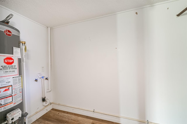 clothes washing area with a textured ceiling, hardwood / wood-style flooring, and water heater