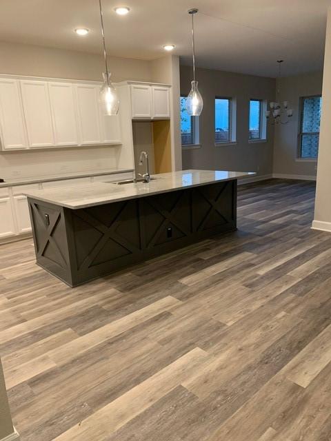 kitchen with a center island with sink, white cabinetry, hanging light fixtures, and sink