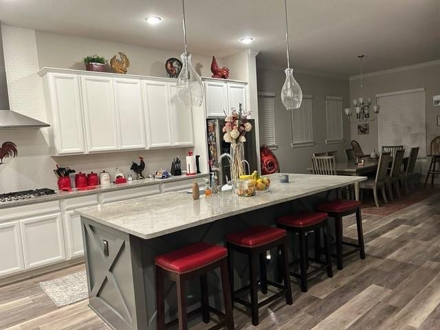 kitchen with white cabinets, stainless steel appliances, an island with sink, and wall chimney exhaust hood