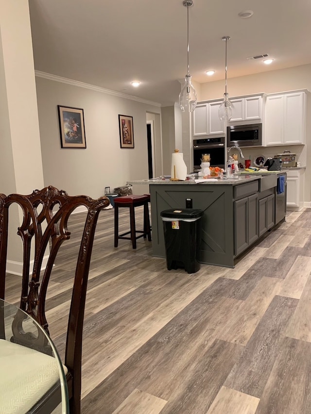 kitchen featuring stainless steel appliances, an island with sink, hanging light fixtures, crown molding, and white cabinetry