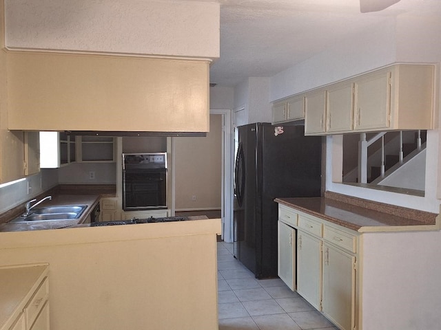 kitchen with cream cabinets, sink, light tile patterned floors, and black appliances