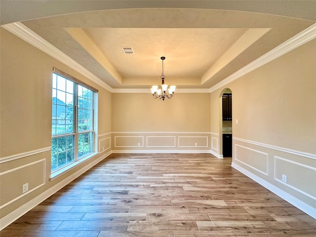 unfurnished dining area with light hardwood / wood-style floors, a raised ceiling, ornamental molding, and a chandelier