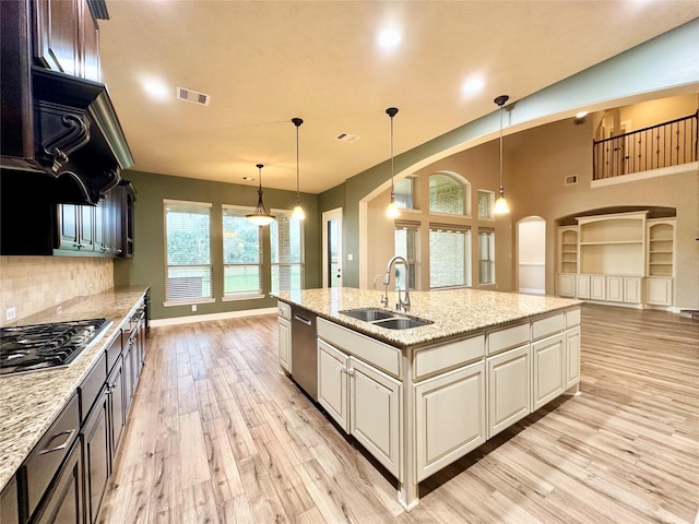 kitchen featuring sink, hanging light fixtures, light stone counters, appliances with stainless steel finishes, and light wood-type flooring