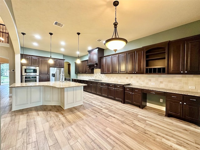 kitchen featuring light hardwood / wood-style flooring, an island with sink, decorative light fixtures, and appliances with stainless steel finishes