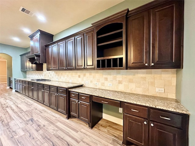 kitchen with dark brown cabinets, light hardwood / wood-style floors, stainless steel gas cooktop, and tasteful backsplash