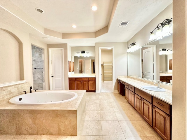 bathroom featuring vanity, tiled bath, and a tray ceiling