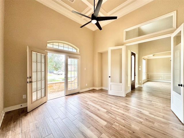 interior space with french doors, light wood-type flooring, ornamental molding, ceiling fan, and a high ceiling