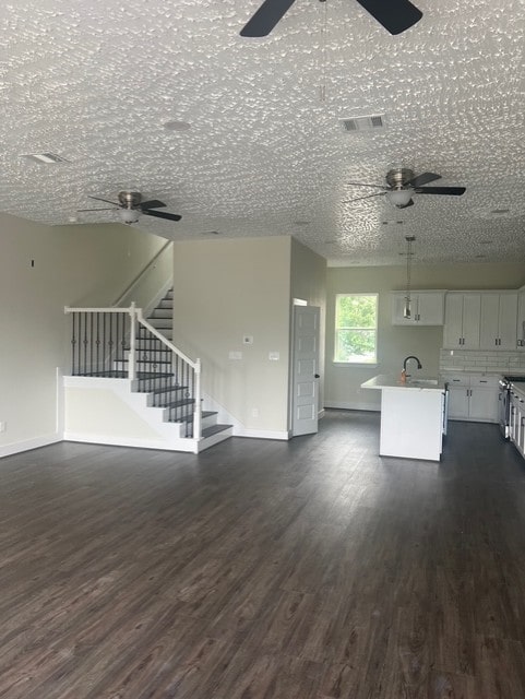 unfurnished living room featuring visible vents, a ceiling fan, dark wood-style flooring, and baseboards