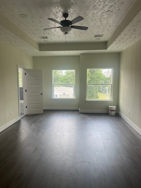 unfurnished room with visible vents, plenty of natural light, a raised ceiling, and dark wood-type flooring