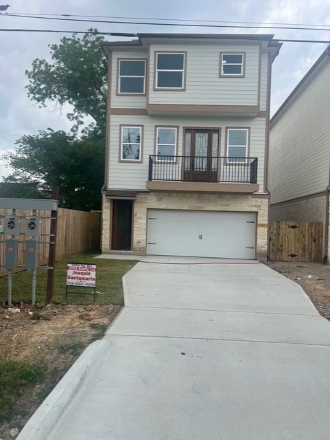 view of front facade featuring fence, an attached garage, concrete driveway, and stone siding
