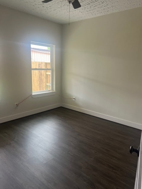 empty room featuring baseboards, ceiling fan, dark wood finished floors, and a textured ceiling