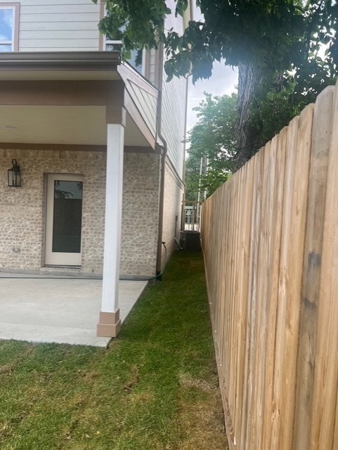 view of side of property featuring fence, a lawn, a patio area, and brick siding