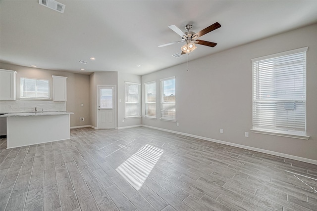 unfurnished living room featuring ceiling fan, sink, and light wood-type flooring