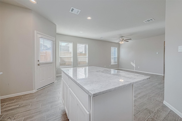 kitchen featuring ceiling fan, a center island, white cabinets, and light stone counters