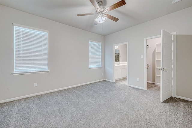 unfurnished bedroom featuring connected bathroom, ceiling fan, light colored carpet, and a spacious closet