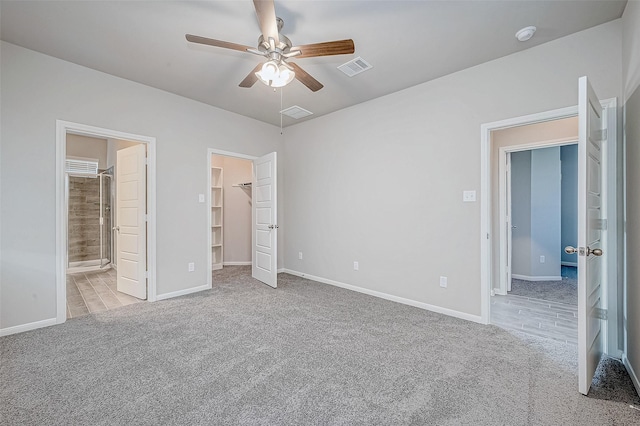 unfurnished bedroom with a spacious closet, ceiling fan, ensuite bathroom, light carpet, and a closet