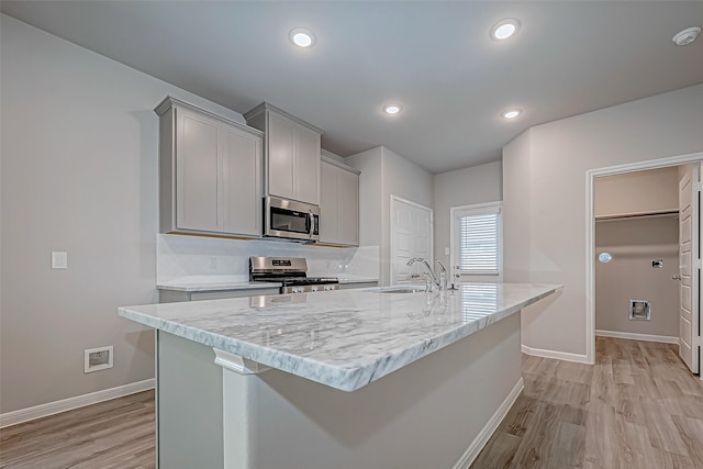 kitchen with appliances with stainless steel finishes, light wood-type flooring, gray cabinets, and a center island with sink