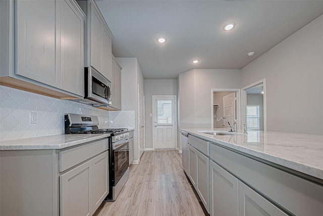 kitchen featuring light stone countertops, sink, stainless steel appliances, tasteful backsplash, and light hardwood / wood-style floors