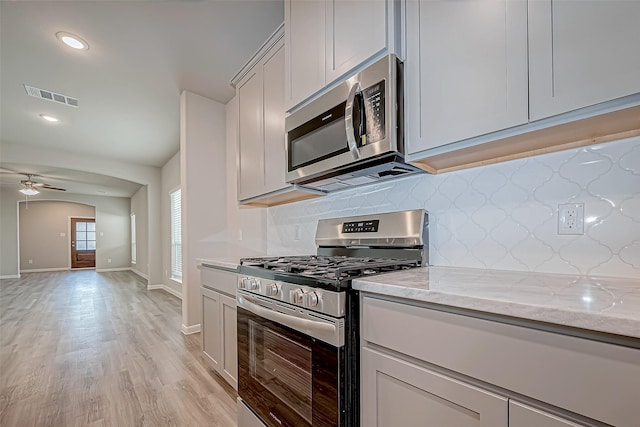 kitchen featuring ceiling fan, decorative backsplash, appliances with stainless steel finishes, light hardwood / wood-style floors, and light stone counters