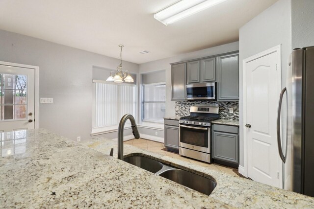 kitchen featuring hanging light fixtures, an inviting chandelier, backsplash, gray cabinets, and appliances with stainless steel finishes