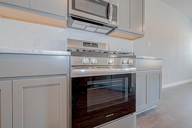 kitchen with decorative backsplash, gray cabinets, stainless steel appliances, and light wood-type flooring