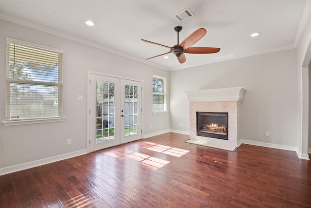 unfurnished living room featuring a tiled fireplace, ceiling fan, french doors, and crown molding