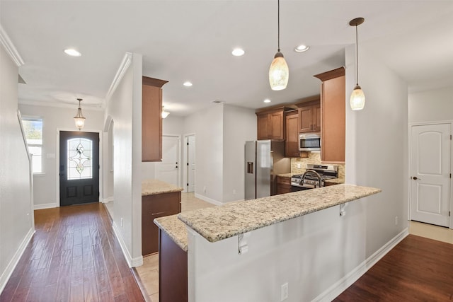 kitchen with kitchen peninsula, appliances with stainless steel finishes, a kitchen bar, and pendant lighting