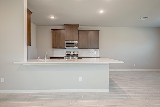 kitchen with backsplash, kitchen peninsula, sink, and appliances with stainless steel finishes