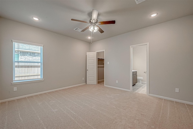 unfurnished bedroom with light carpet, ensuite bathroom, ceiling fan, a spacious closet, and a closet