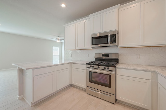 kitchen with ceiling fan, light stone counters, kitchen peninsula, white cabinets, and appliances with stainless steel finishes