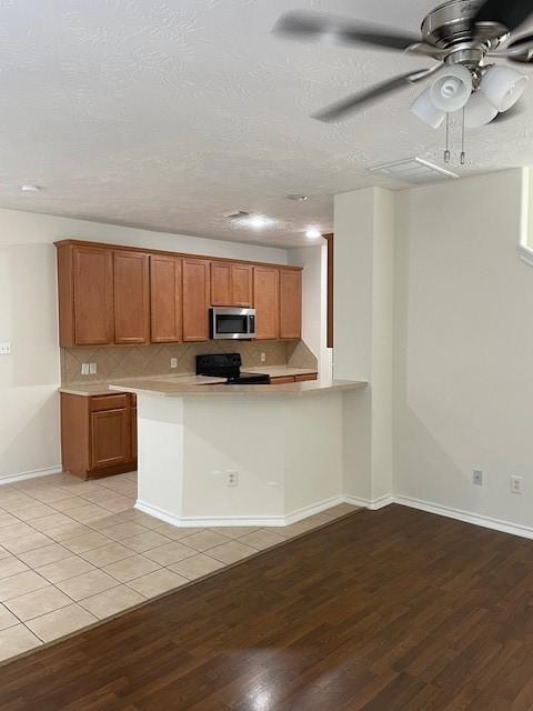 kitchen featuring ceiling fan, black range oven, kitchen peninsula, light hardwood / wood-style floors, and decorative backsplash