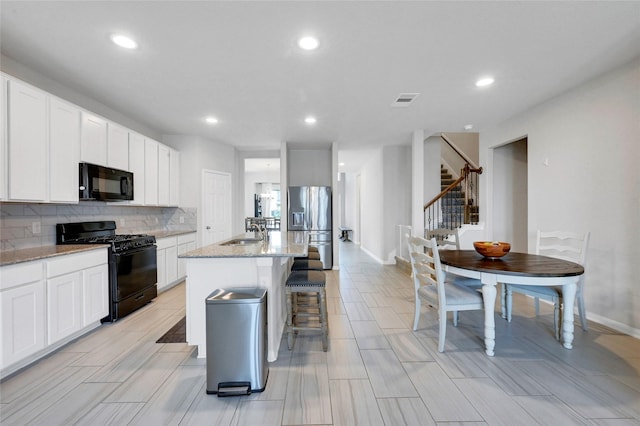 kitchen with light stone countertops, sink, white cabinetry, a kitchen island with sink, and black appliances