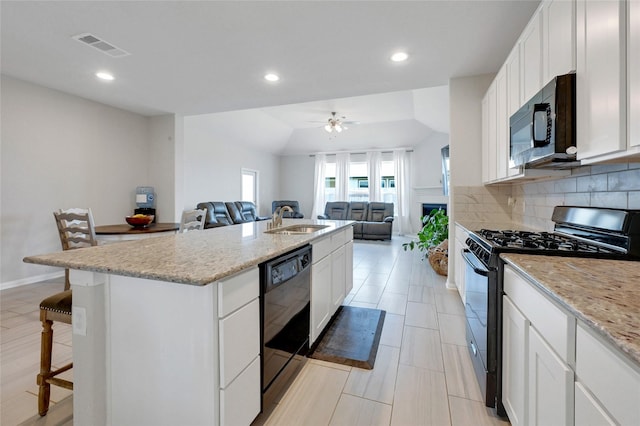 kitchen with black appliances, white cabinets, sink, and a kitchen island with sink