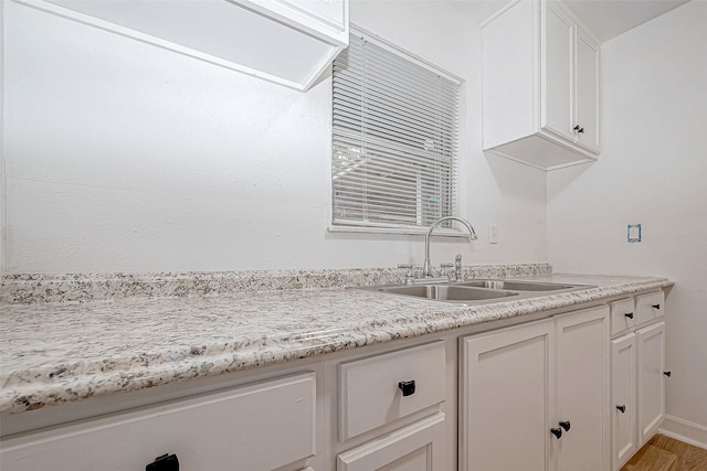 kitchen with light stone countertops, light wood-type flooring, white cabinetry, and sink