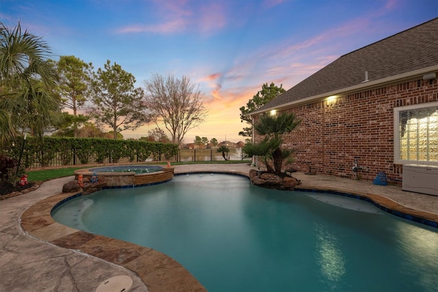 pool at dusk with an in ground hot tub and a patio