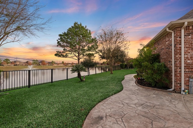 yard at dusk with a water view and a patio