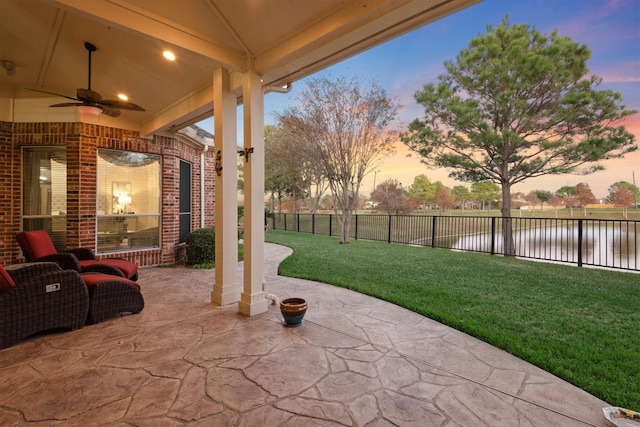 patio terrace at dusk featuring a yard, a water view, and ceiling fan