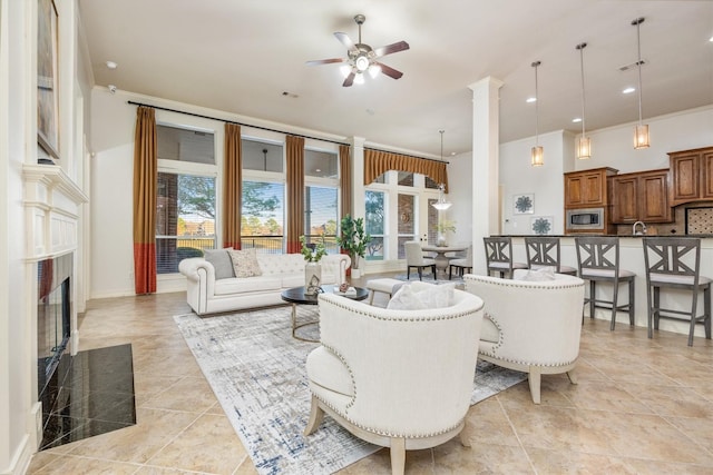 living room with ceiling fan, ornate columns, crown molding, and a high end fireplace