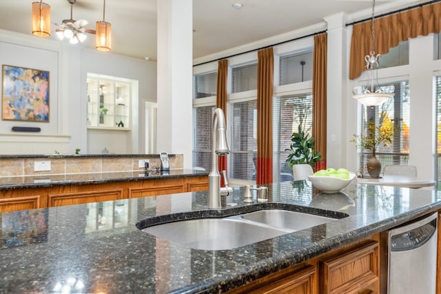 kitchen with stainless steel dishwasher, ceiling fan, sink, dark stone countertops, and hanging light fixtures