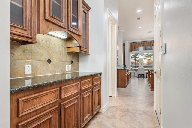 kitchen featuring pendant lighting, dark stone countertops, ornamental molding, and tasteful backsplash