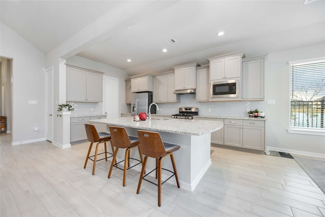 kitchen featuring a kitchen bar, stainless steel appliances, a center island with sink, and lofted ceiling