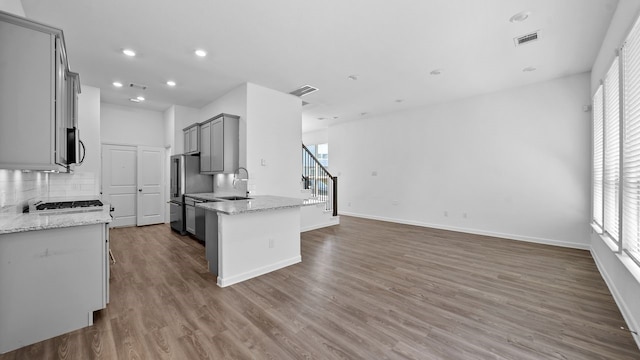 kitchen with light stone countertops, backsplash, sink, hardwood / wood-style flooring, and gray cabinets