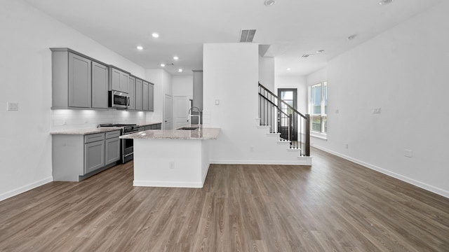 kitchen with gray cabinetry, hardwood / wood-style floors, backsplash, light stone countertops, and stainless steel appliances